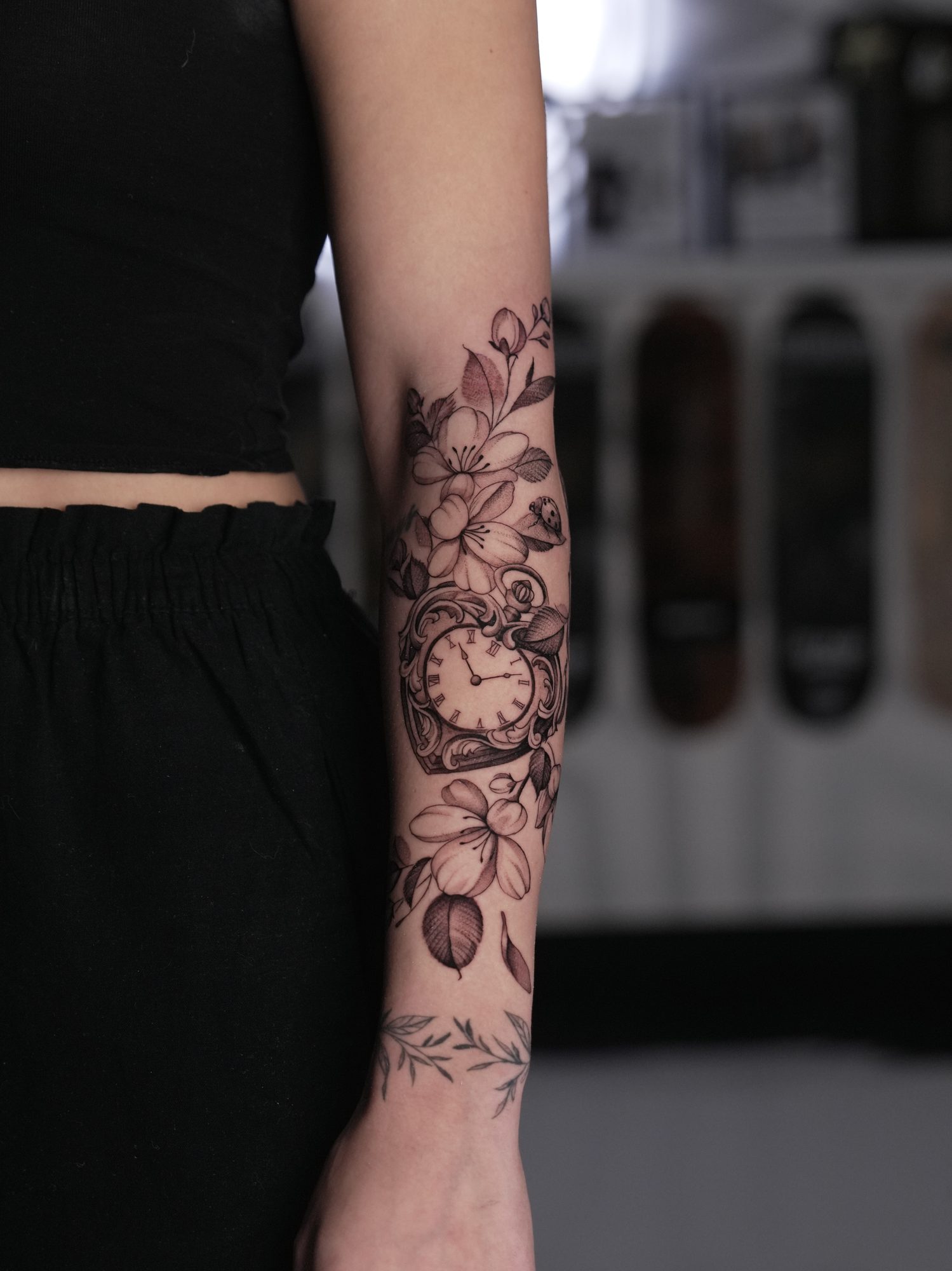 Fine line floral forearm tattoo with a vintage pocket watch in black and grey