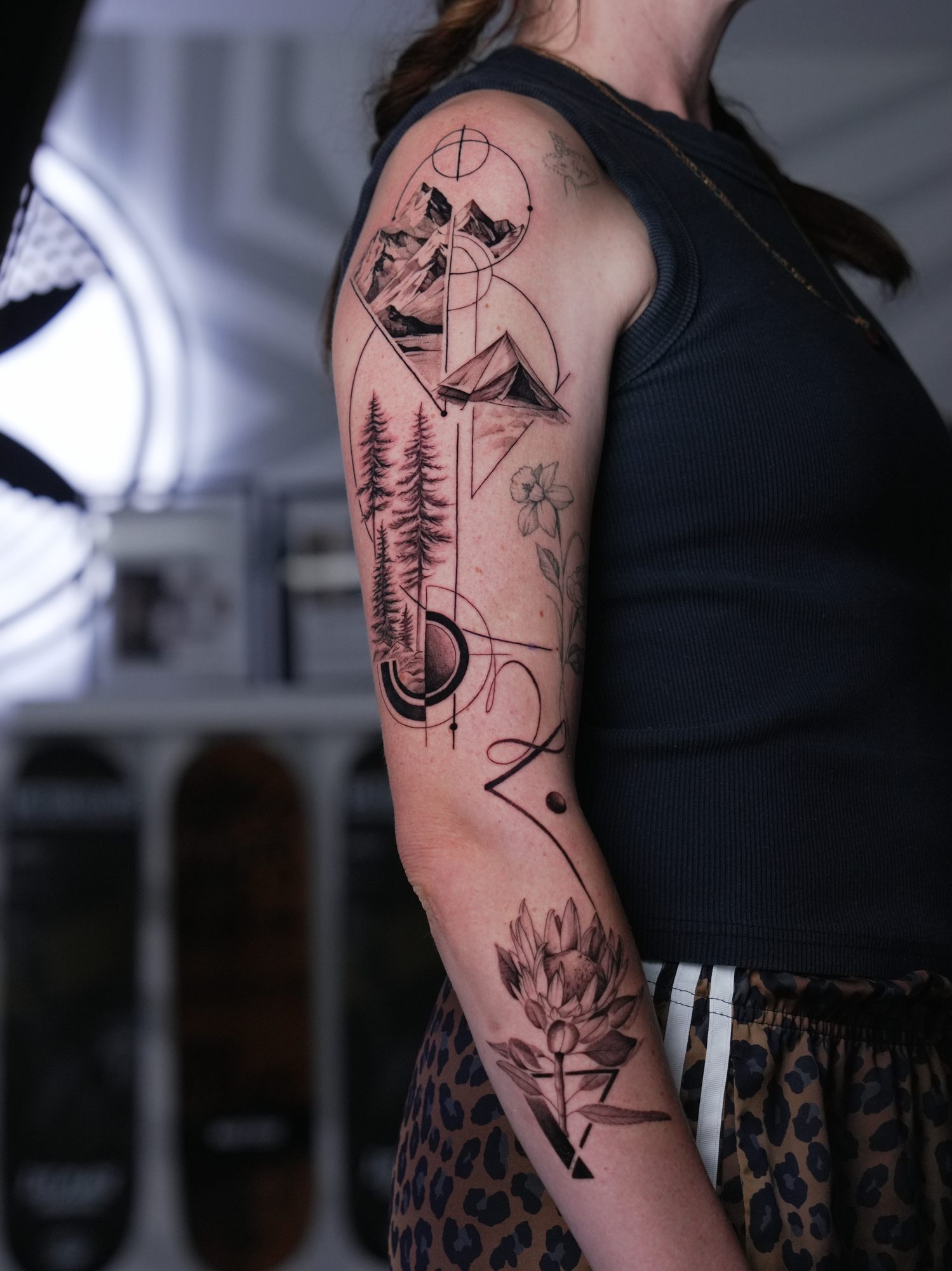 Geometric black and grey sleeve with mountains, pine forest and a protea — nature woven into sacred geometry