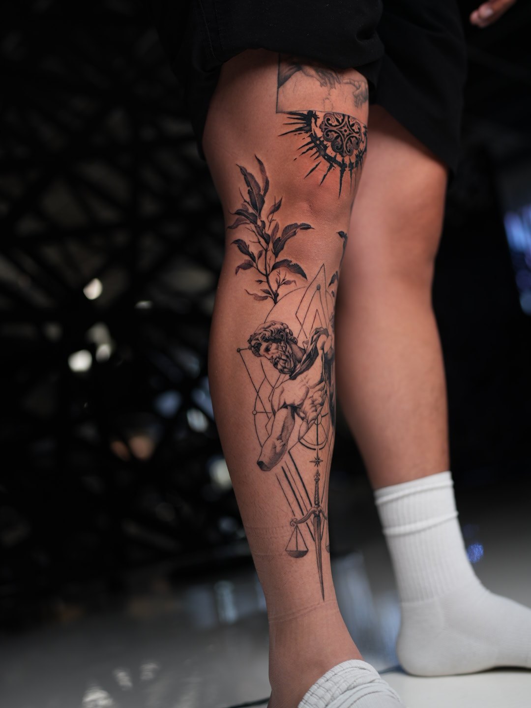 Black and grey geometric leg tattoo — Greek mythological figure with olive branch and ornamental mandala