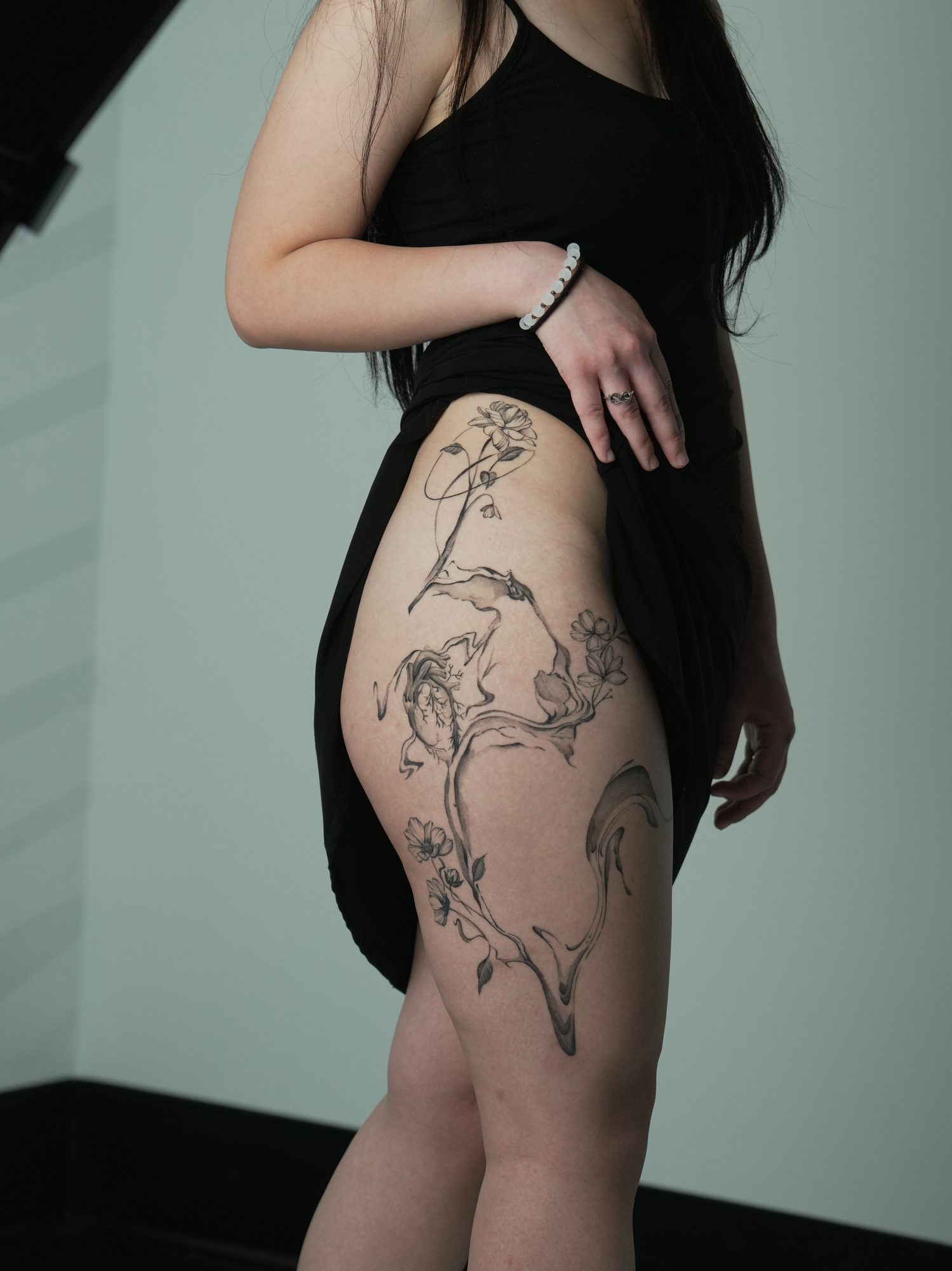 Flowing ink wash and fine line flowers along the hip and thigh in black and grey